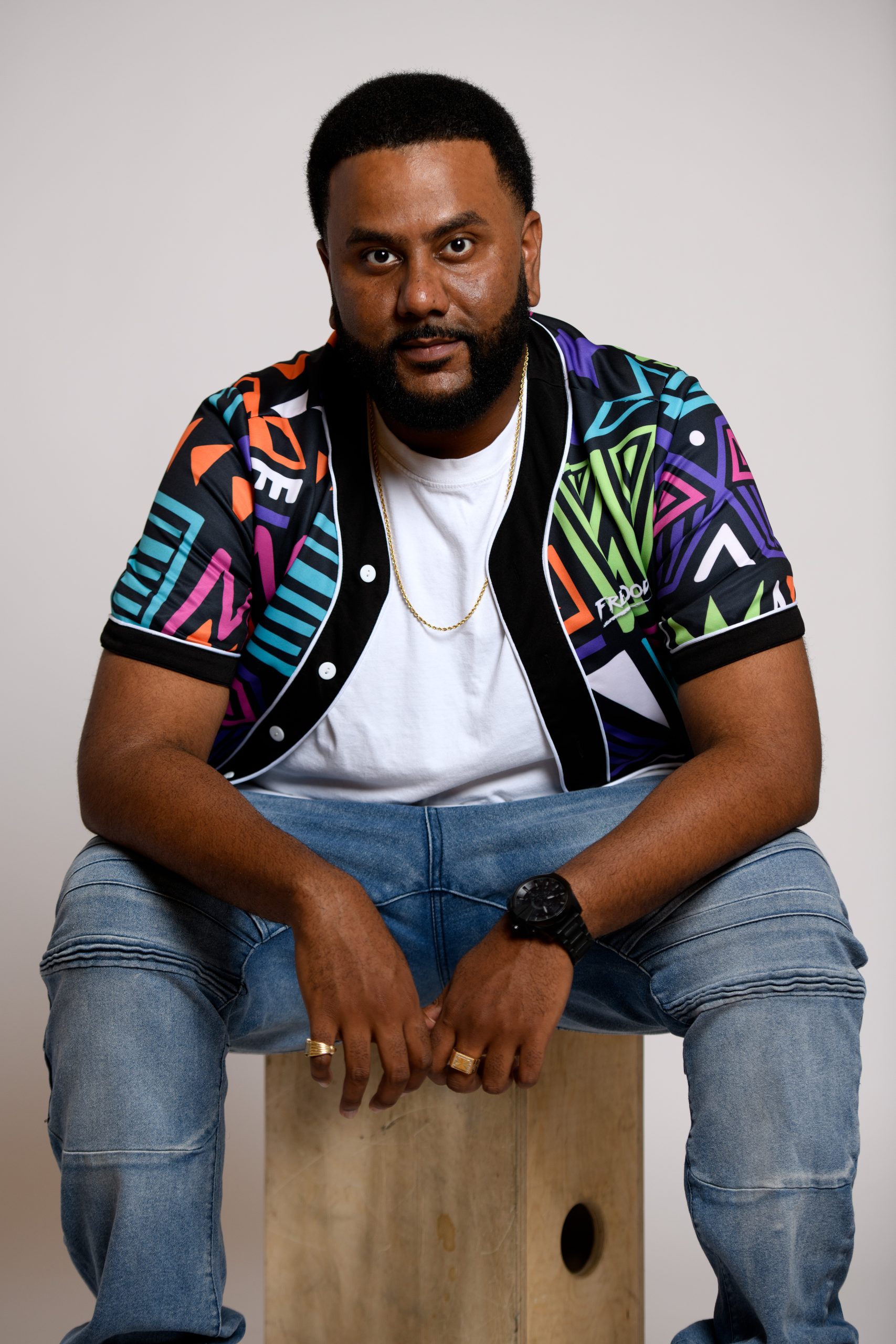 Studio portrait of Toronto DJ, MC and promoter DJ BuzzB seated in a multicolored patterned shirt