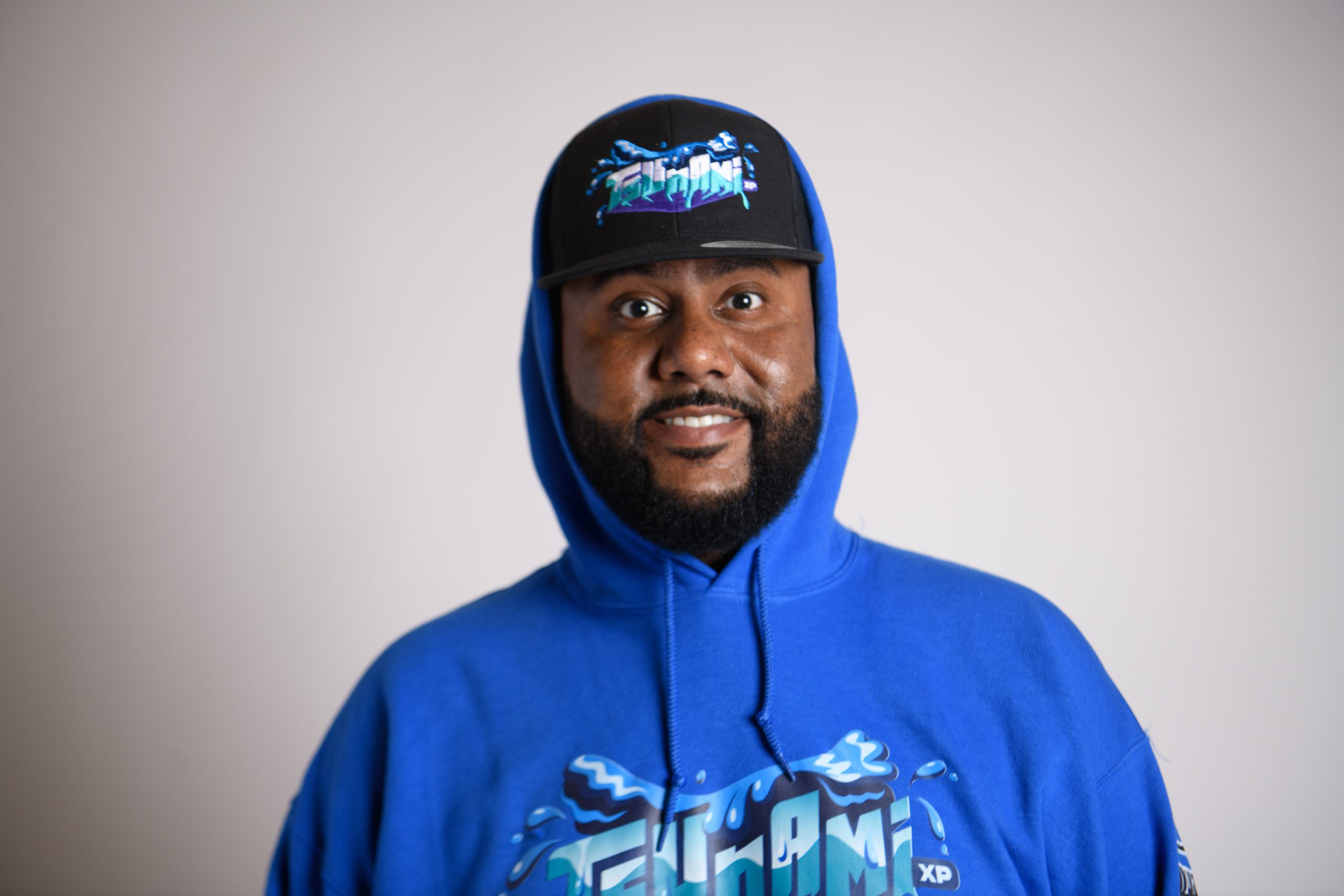 Studio portrait of DJ BuzzB wearing a blue Tsunami hoodie and black cap