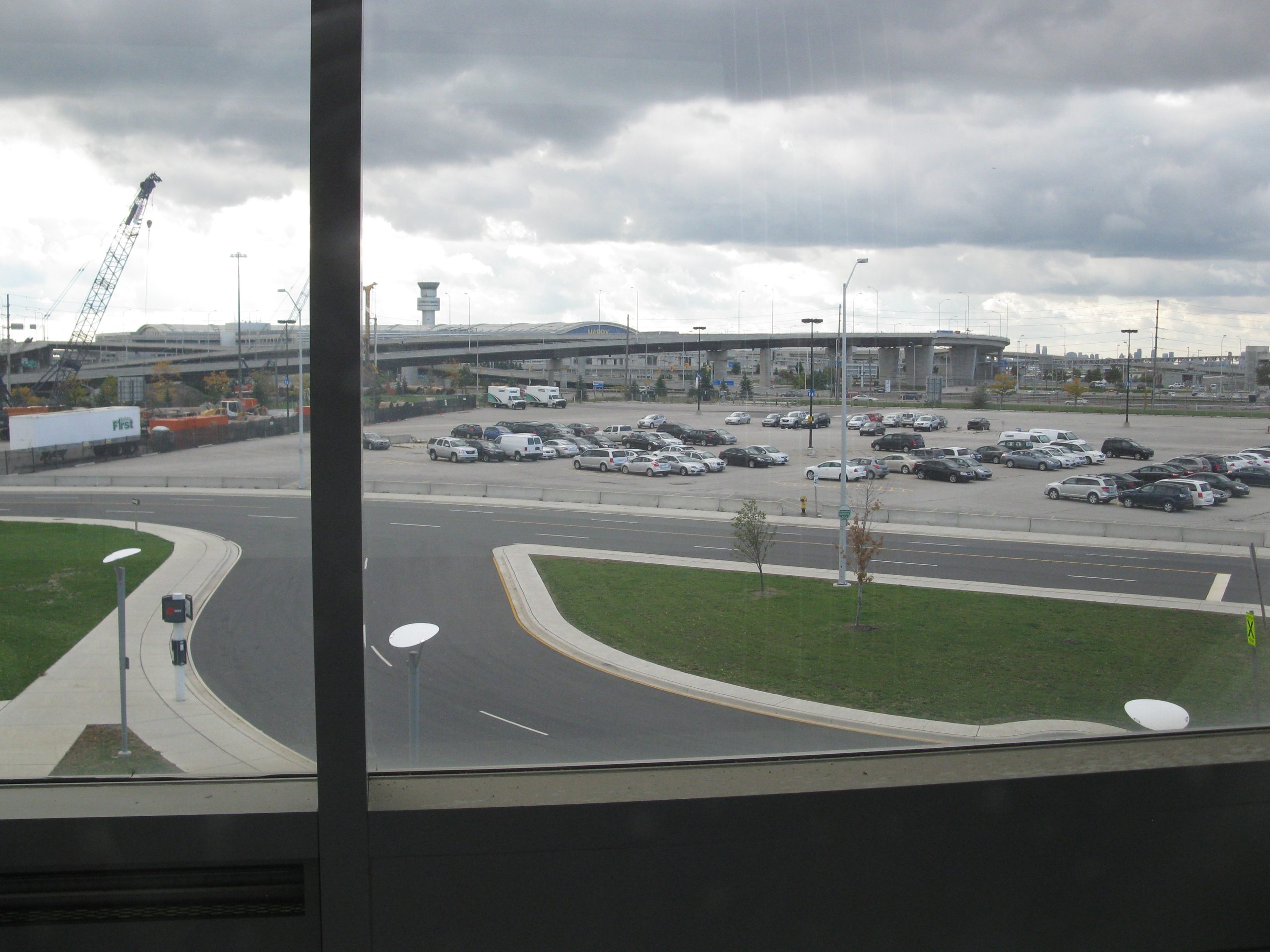 View from the interterminal tram at Toronto Pearson International Airport, looking across airport roads and parking toward the terminal.